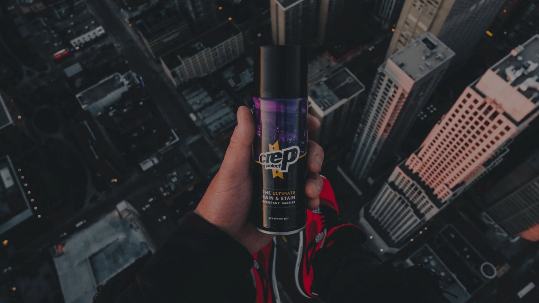 Crep Protect Rain & Stain spray held up over a city skyline